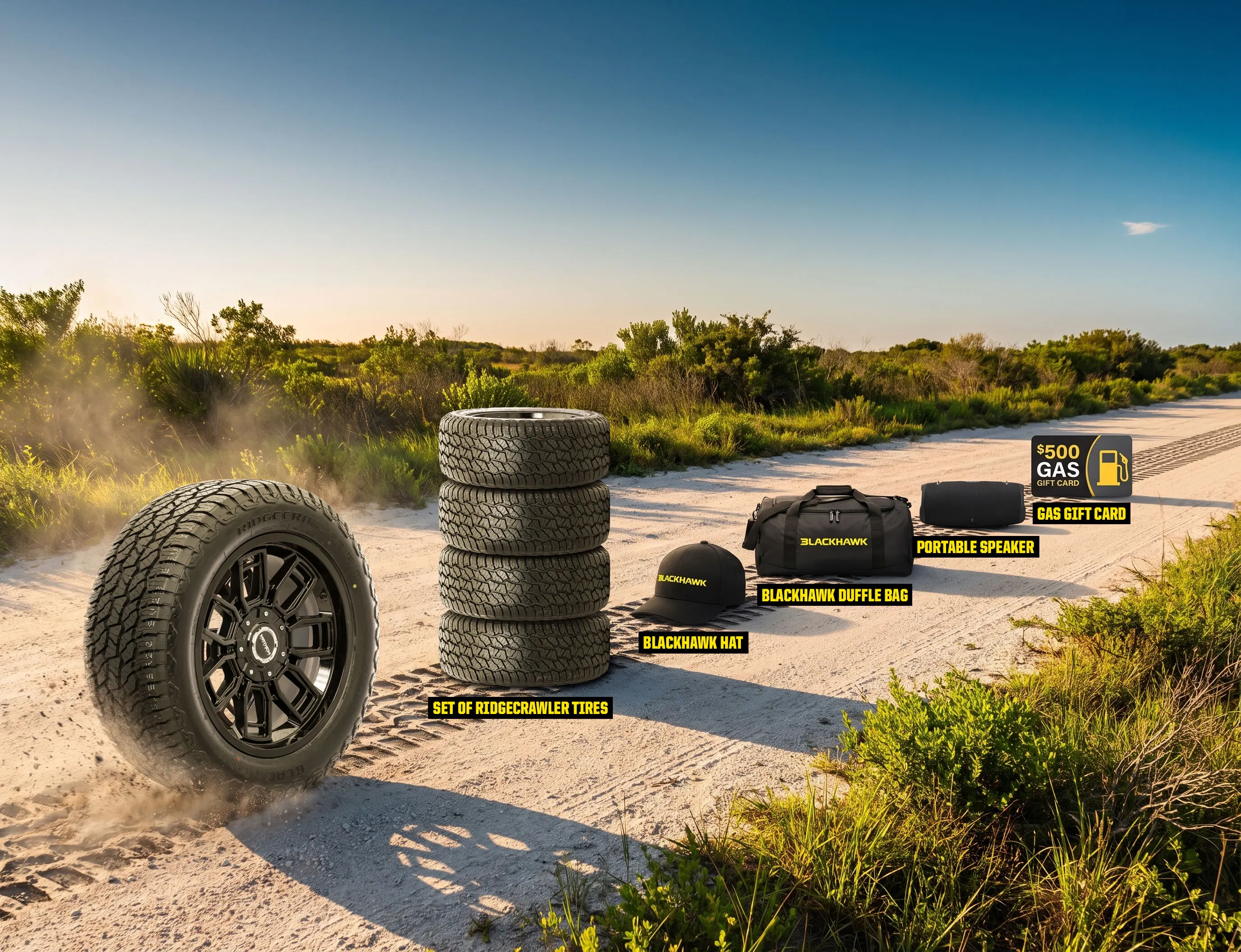 Prize reveal image showing a Blackhawk Ridgecrawler tire on a sandy off-road trail with a set of four Ridgecrawler tires and Blackhawk-branded prizes arranged beside it. Prizes include a Blackhawk hat, duffle bag, portable speaker, and a $500 gas gift card, with each item labeled. Green shrubs and a clear blue sky form the background, emphasizing an outdoor adventure theme.