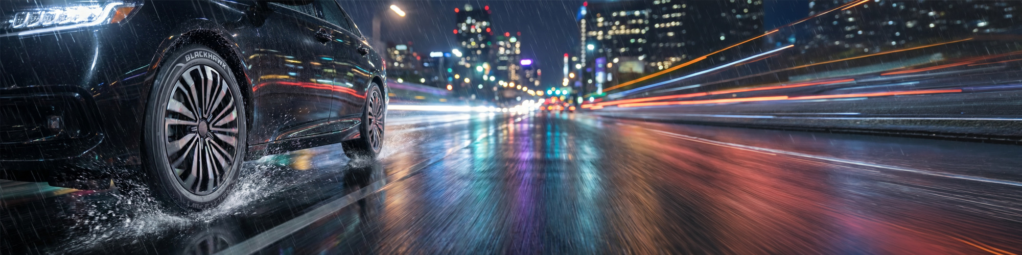 Blackhawk Agility AWT tire on car driving through wet city street at night with water spray and reflections